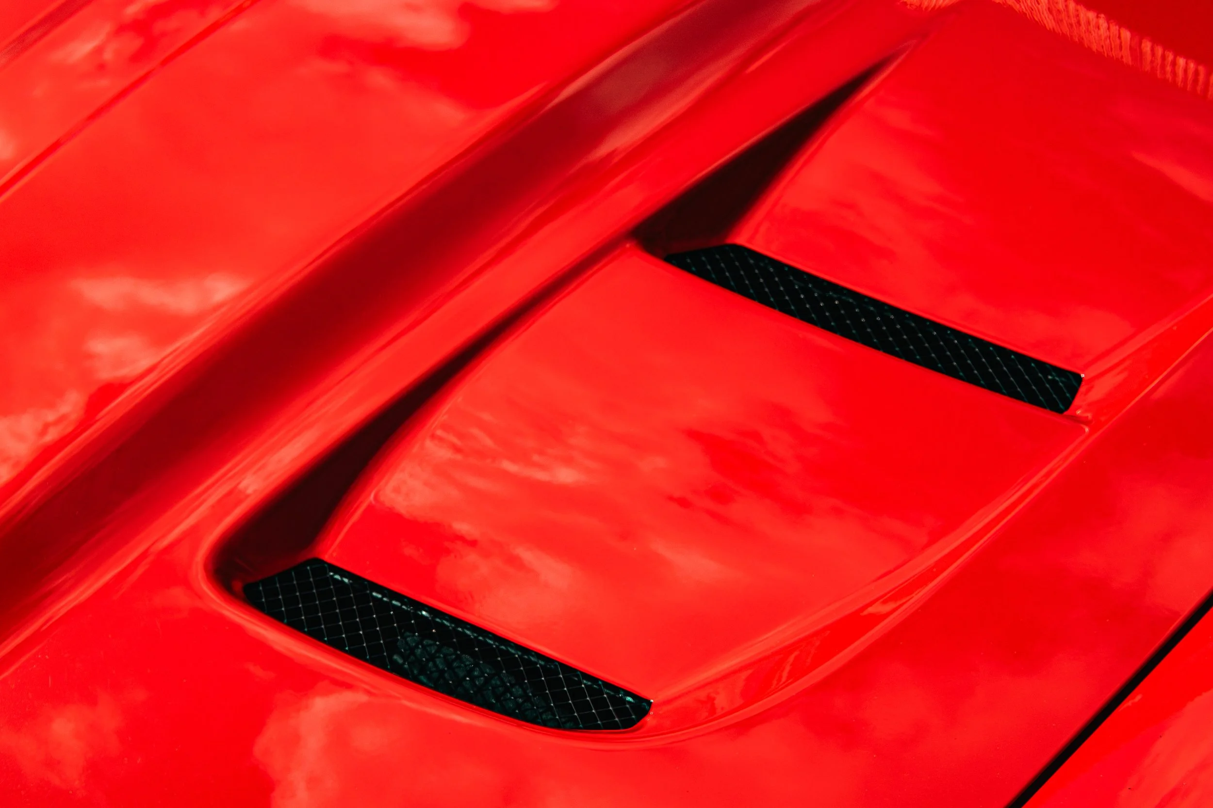 Close-up of a red sports car hood with black vents and reflective surface.