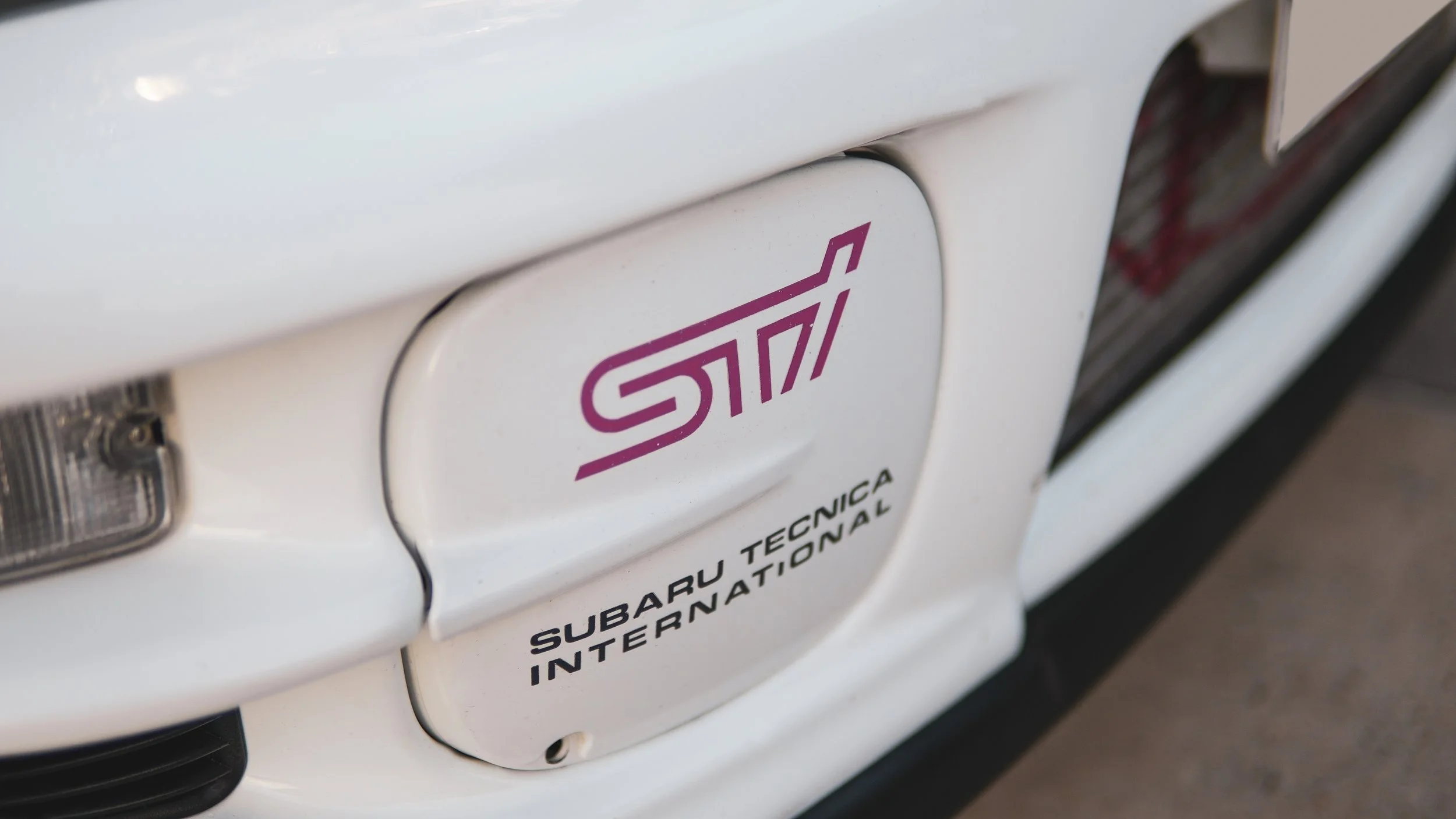 Close-up of a white car with a Subaru STI badge and a sticker that says SUBARU TECNICA INTERNATIONAL.