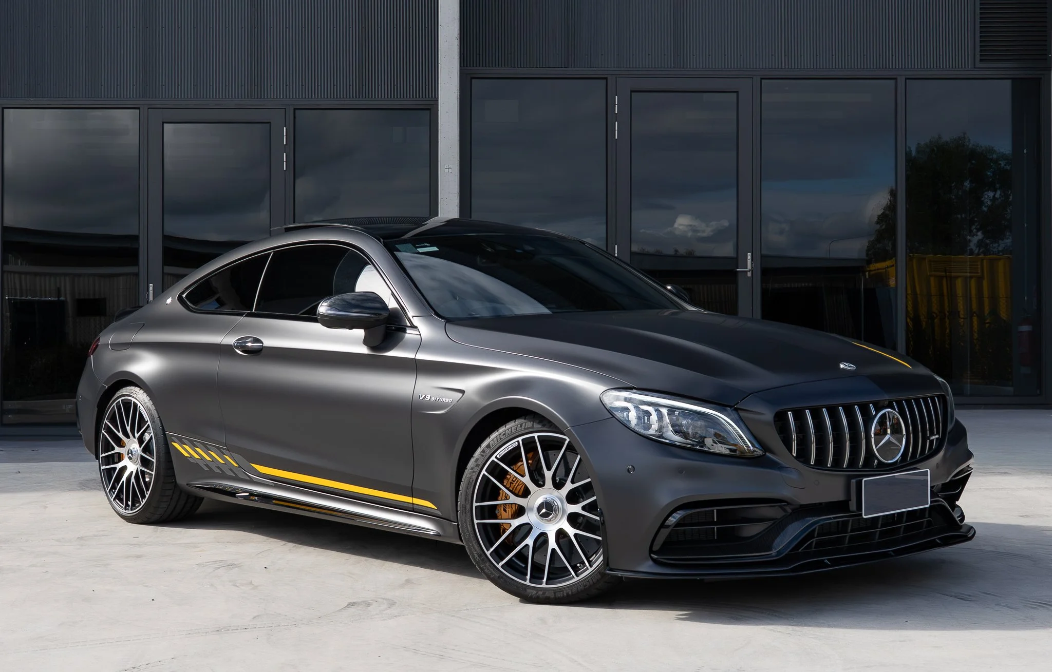 Gray Mercedes-Benz coupe with yellow stripe parked in front of building with glass windows