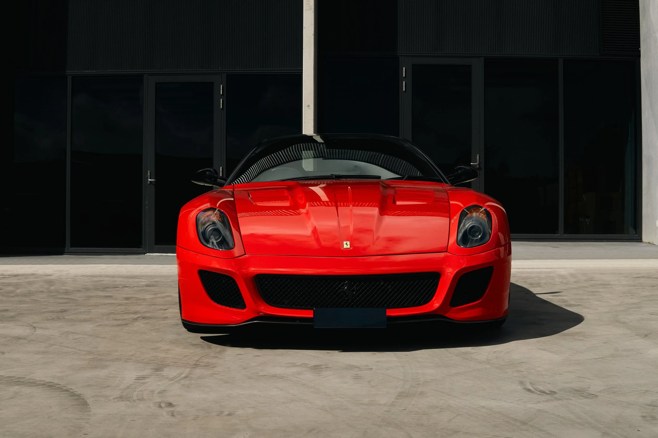 Red Ferrari sports car parked in front of a modern building with large black tinted windows.