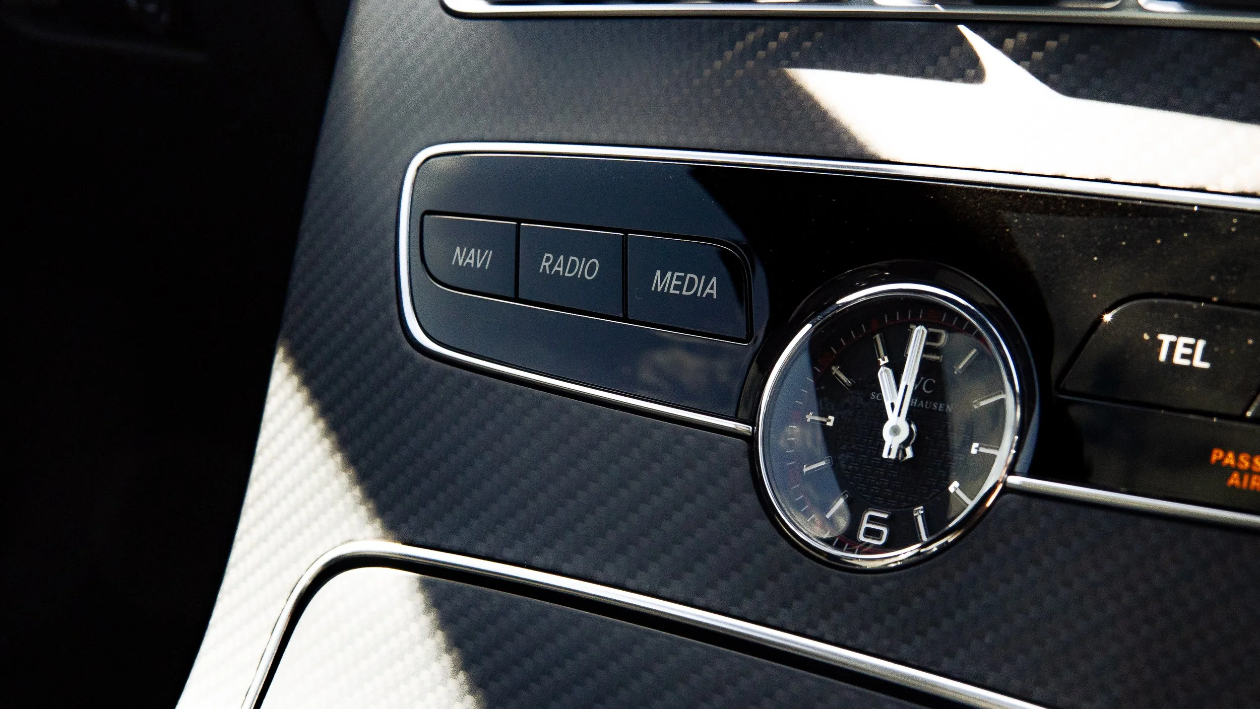 Close-up of a car's dashboard showing navigation, radio, media buttons, an analog clock, and a passenger airbag indicator.
