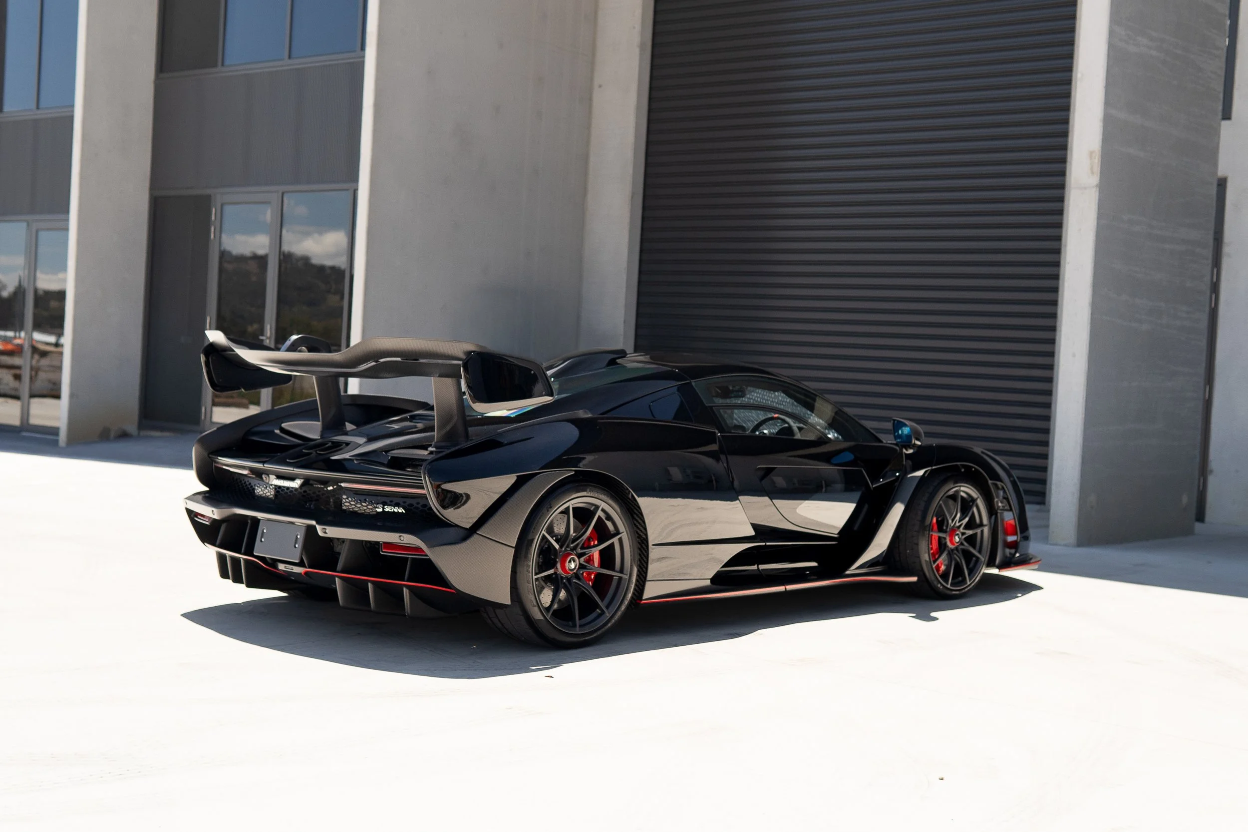 Black McLaren Senna car with red brake callipers parked outside modern building.