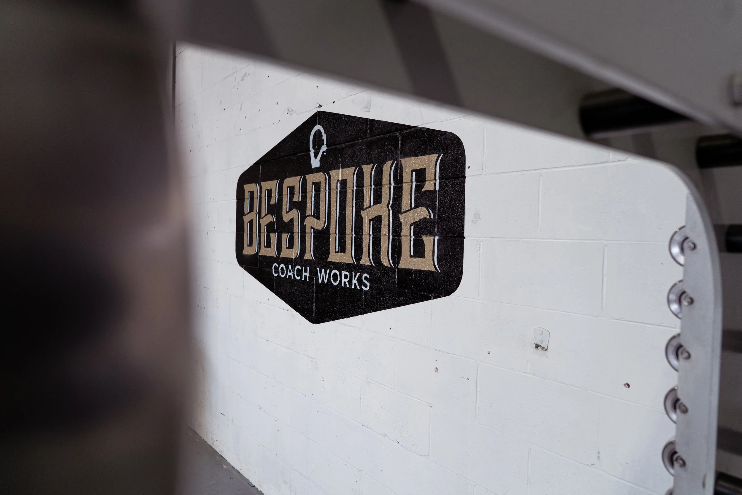 Black and beige sign on a white brick wall reads 'Bespoke Coach Works' with an arrow and a lock symbol above.