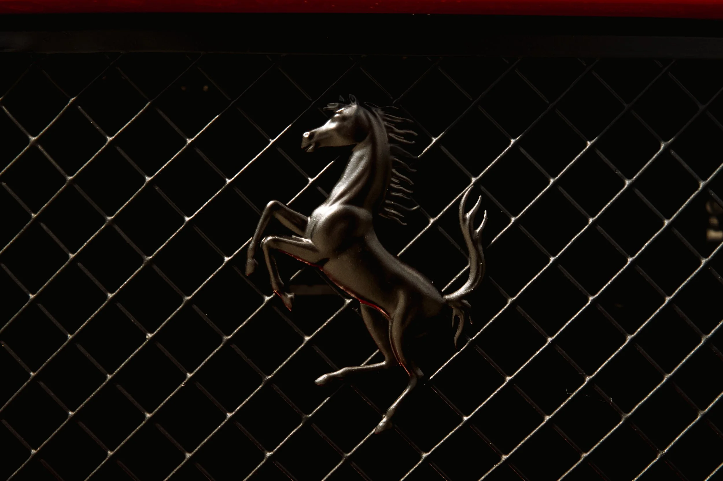 Close-up of a silver prancing horse emblem on a black grill with a red strip at the top.