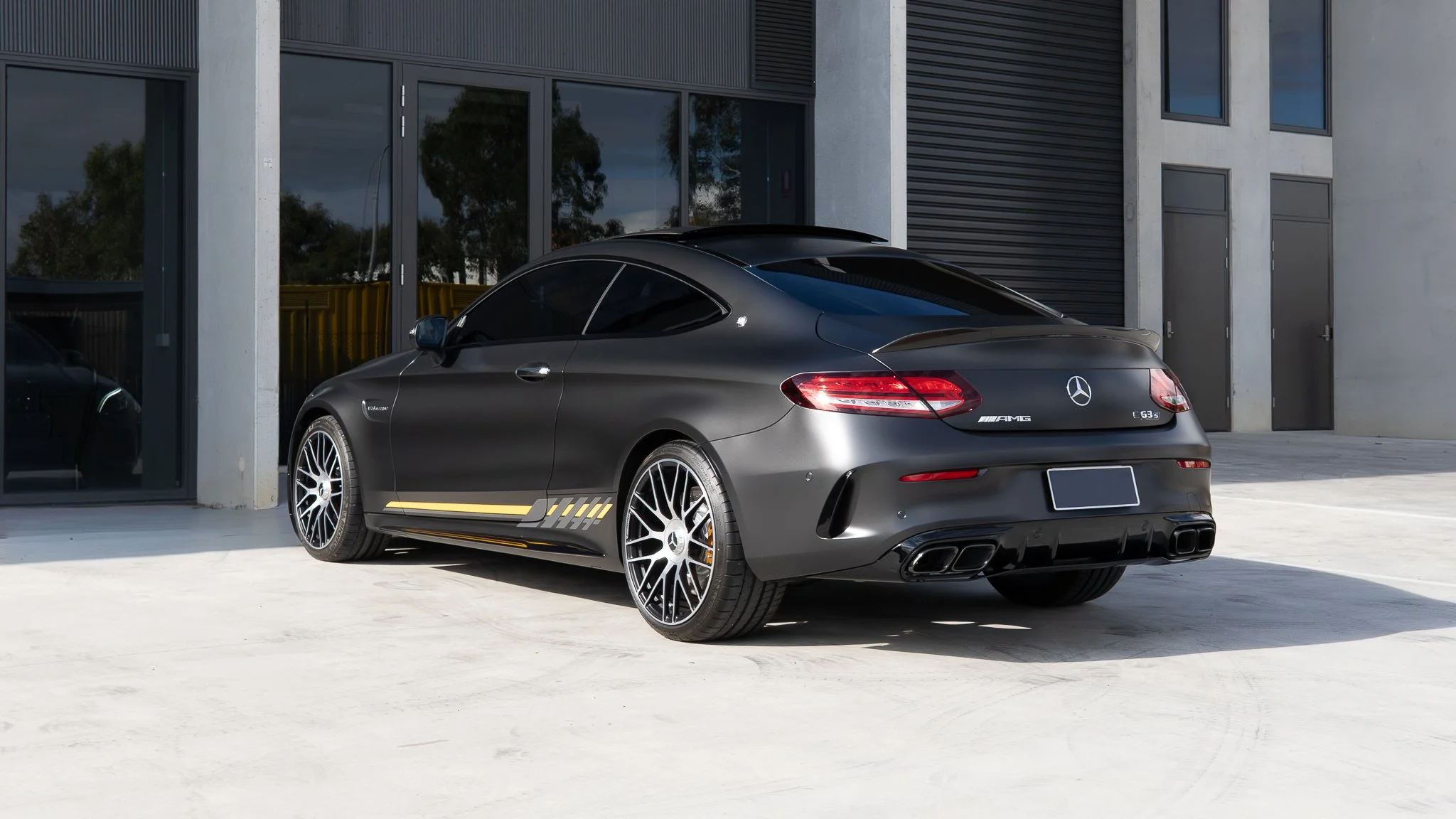 A matte black Mercedes-Benz AMG G63 S coupe parked outside a modern building with large glass windows and concrete walls.