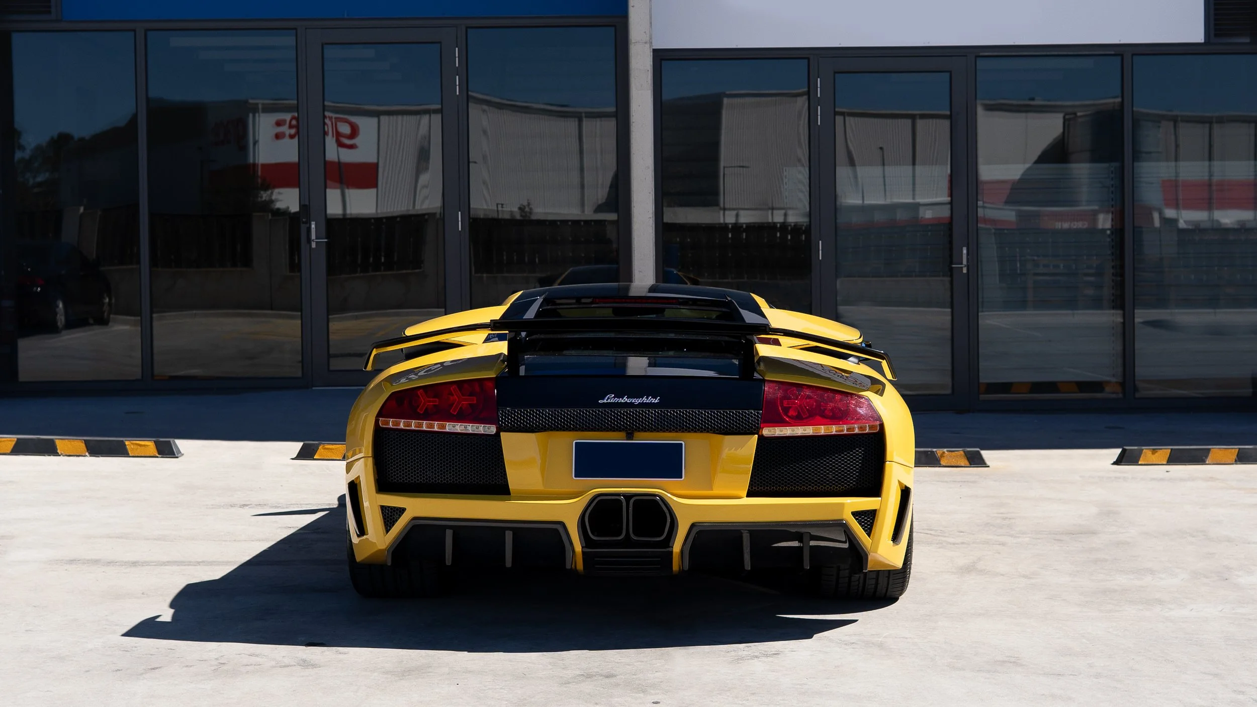 Yellow Lamborghini sports car parked outside a building with large glass doors.