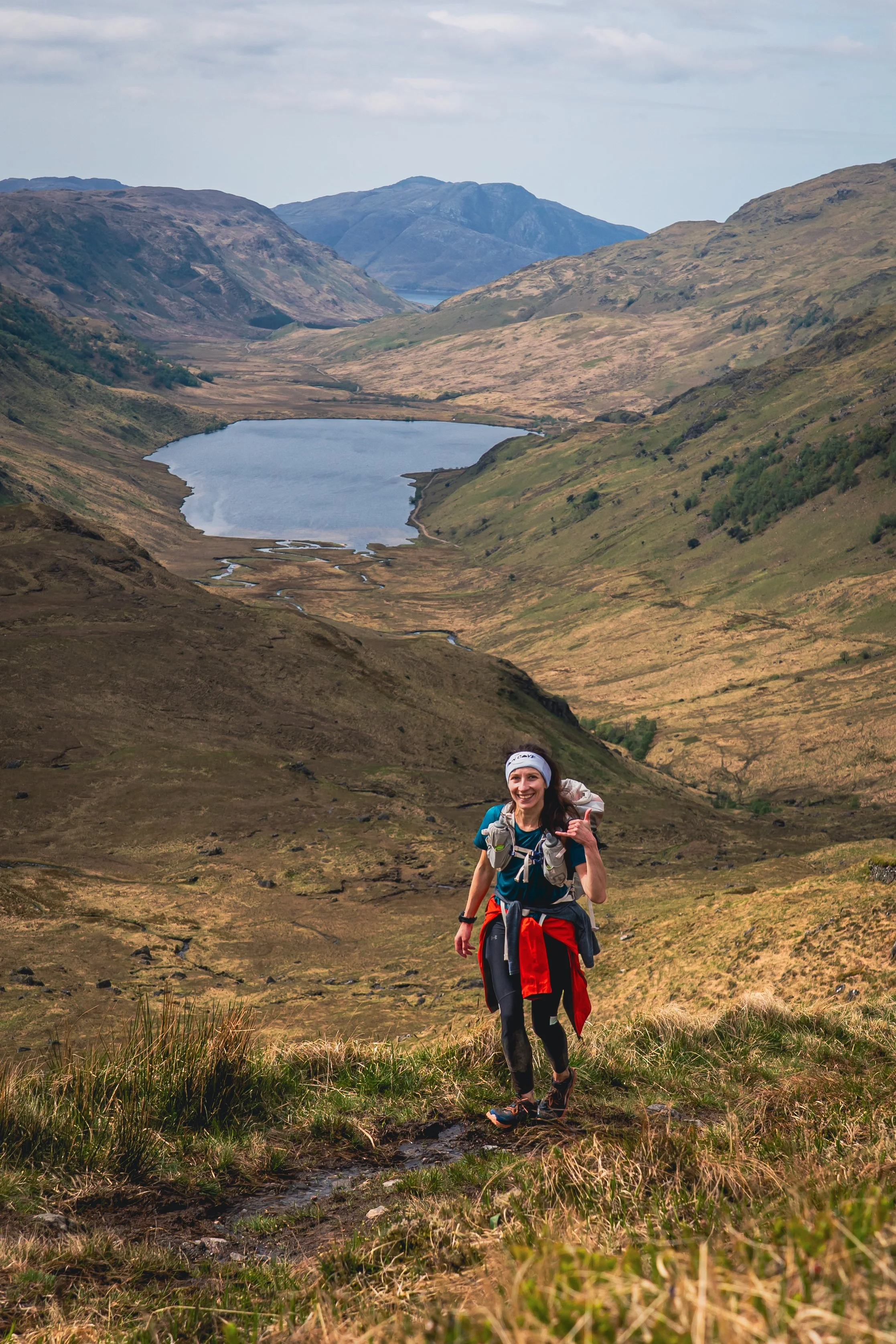 A woman hiking on a trail in a mountainous area with a lake and rolling hills in the background.