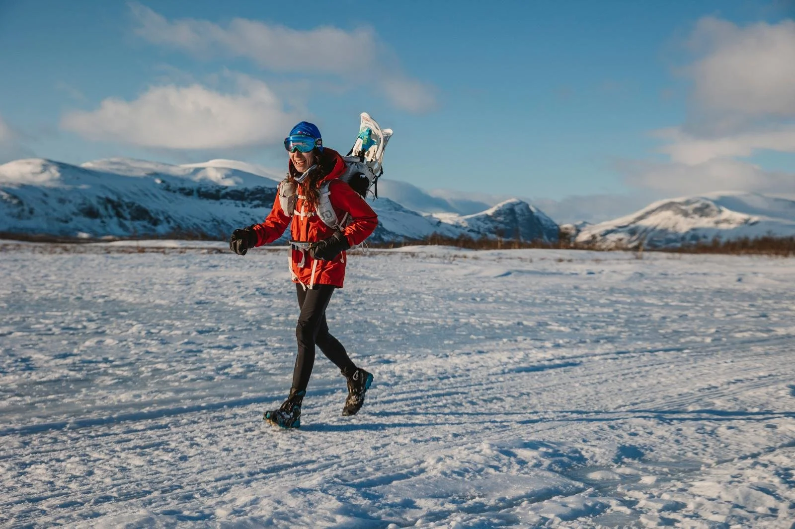 A woman in winter gear running in a snowy landscape with mountains in the background. Arctic Circle -40C