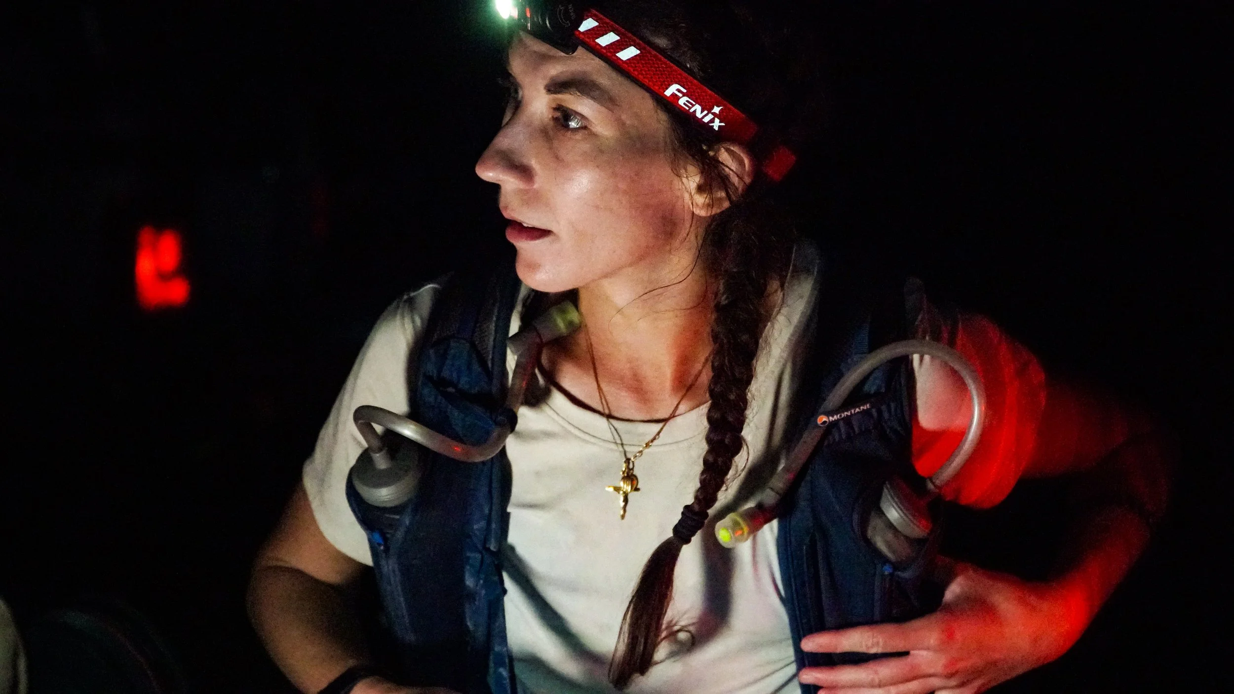 A woman with a headlamp and a backpack in a dark environment, night race.