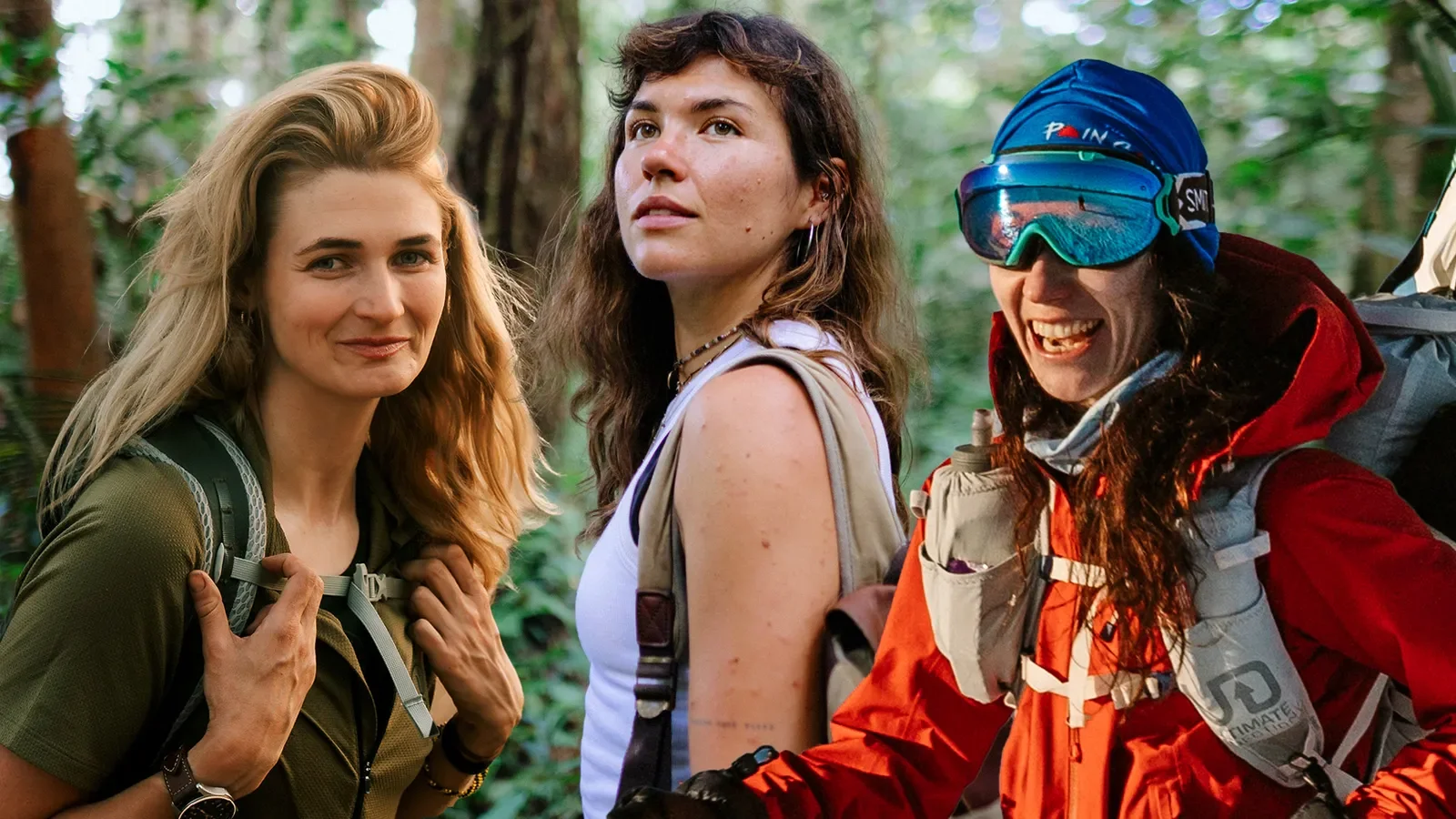 Three women standing in a forest, dressed in outdoor hiking gear, smiling and looking at the camera.