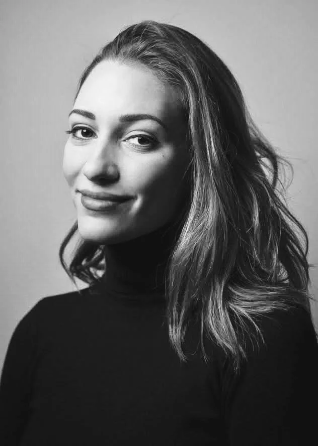 A black-and-white portrait of a woman with wavy hair, wearing a turtleneck top, and smiling slightly at the camera.