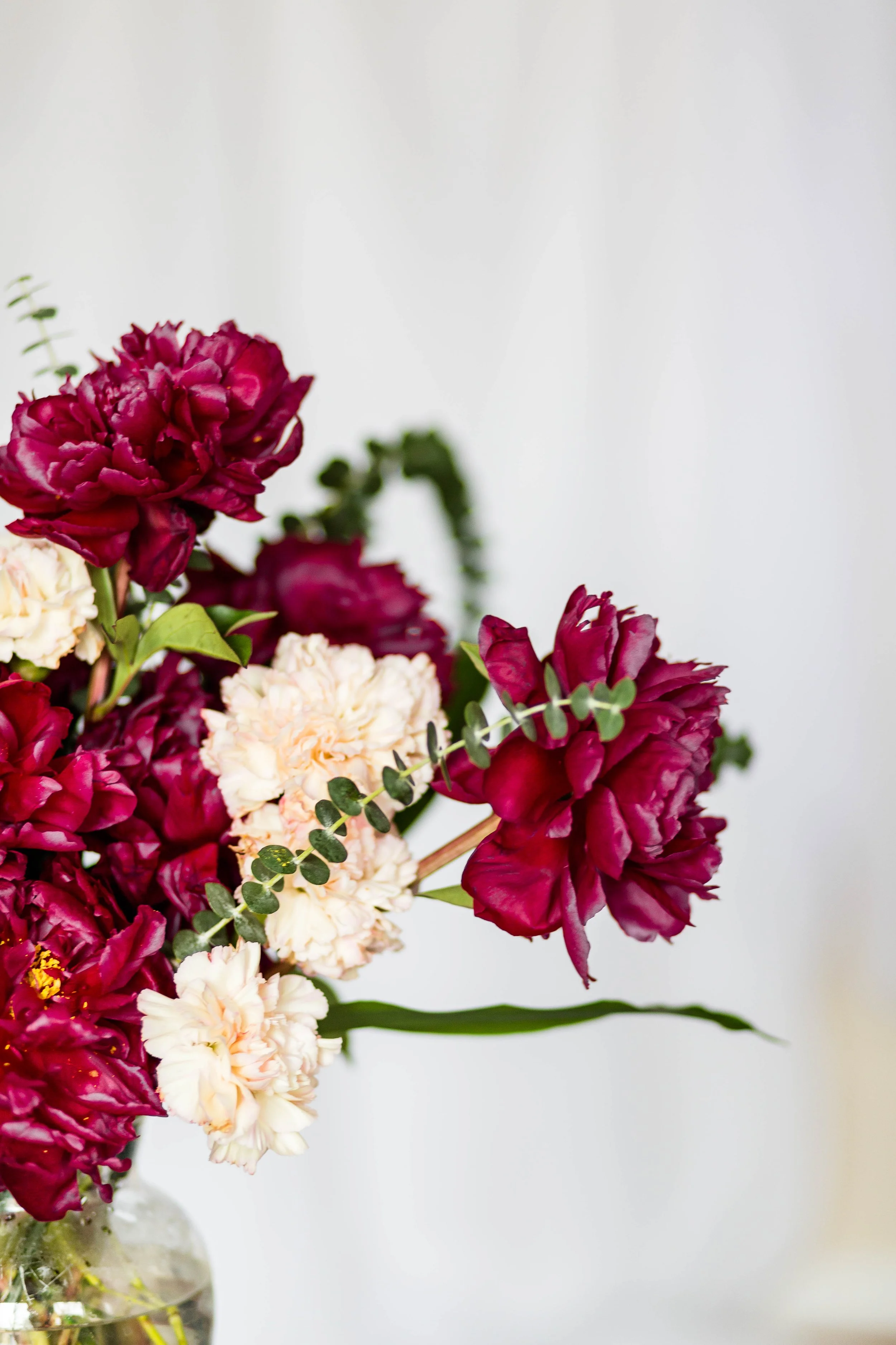 Decorative floral arrangements with greenery and pink accents on a light textured surface, with a torn piece of beige paper in the center.