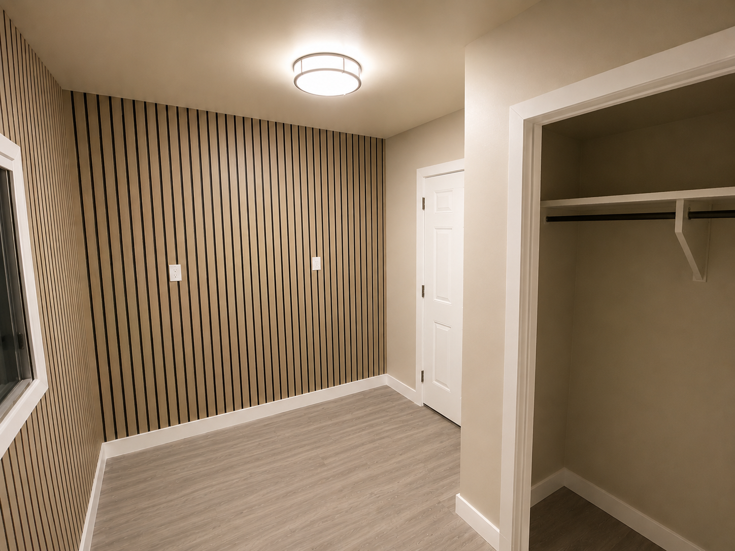 Empty room with a wooden slat accent wall, white door, open closet with a shelf and hanging rod, and a window, with a ceiling light and light-colored flooring.