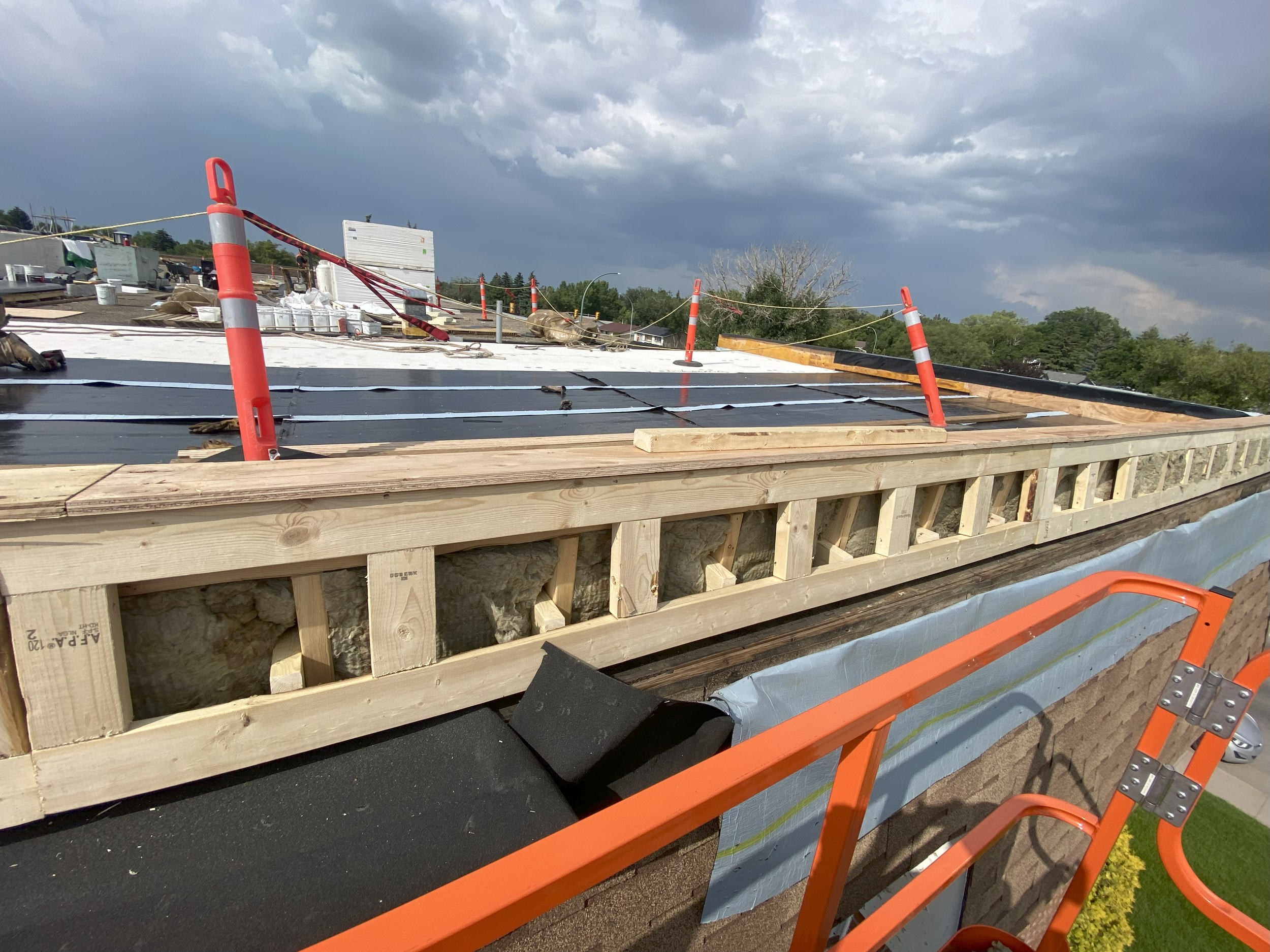 Construction site roof with scaffolding, safety cones, and ropes, under a cloudy sky.