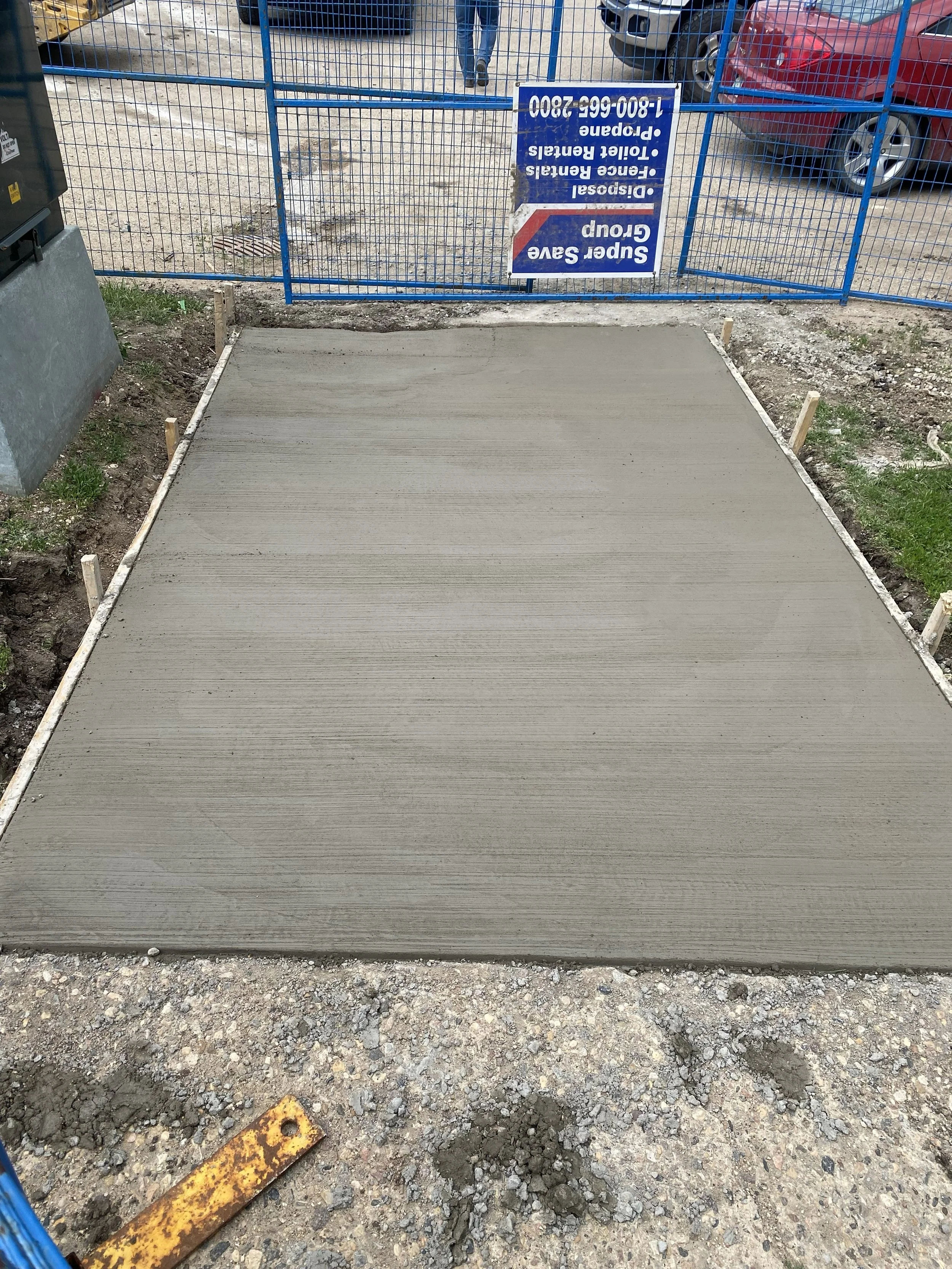 Freshly poured concrete on a sidewalk, with small wooden stakes on the sides and construction debris around.