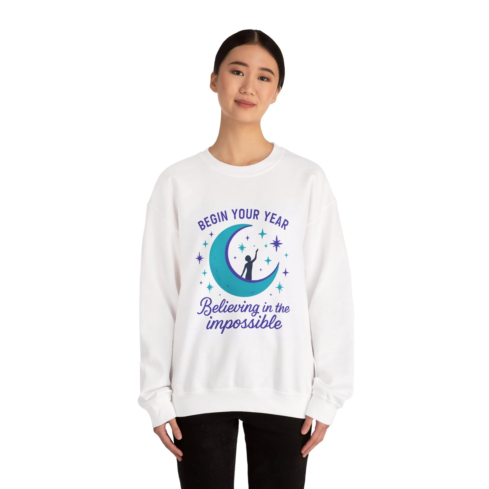 Young woman wearing a white sweatshirt with a moon and stars graphic, the text 'Begin Your Year Believing in the Impossible'