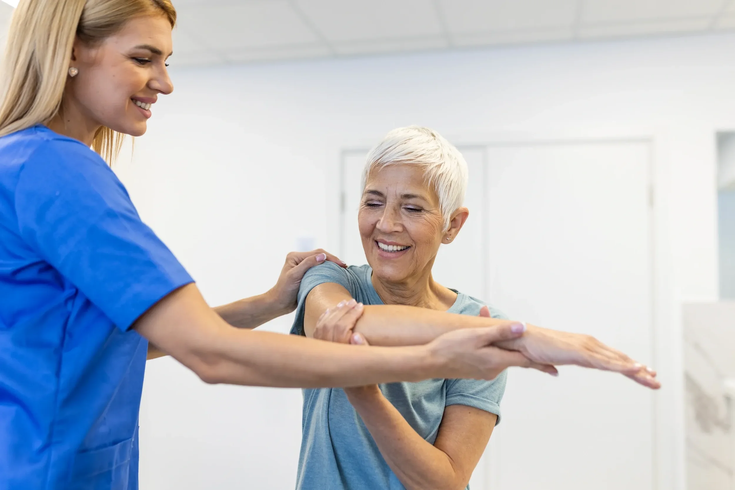 A healthcare worker helping an elderly woman stretch her arm during physical therapy.