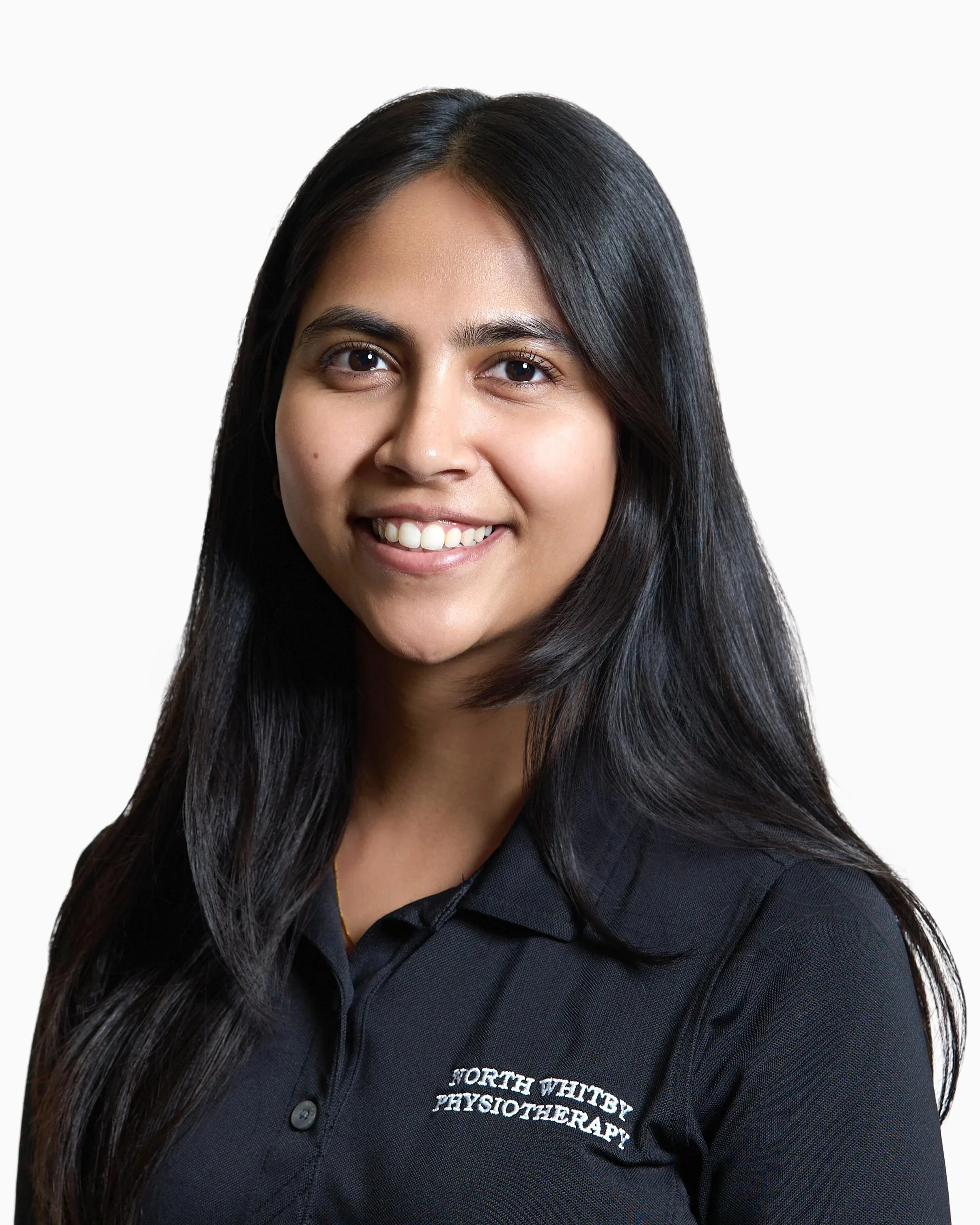 Portrait of a young woman with long dark hair wearing a black polo shirt with 'North Whitby Physiotherapy' embroidered on it, smiling against a white background.