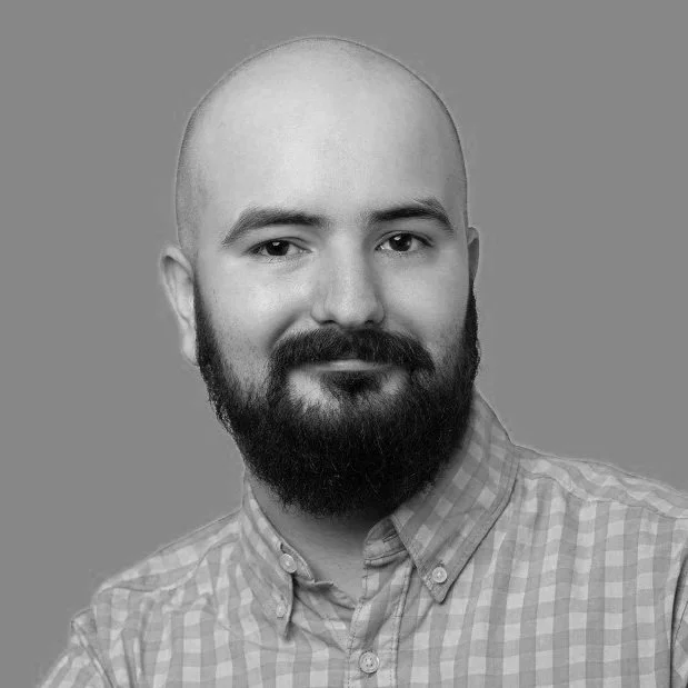 Black and white portrait of a man with a bald head and full beard, wearing a checkered button-up shirt.