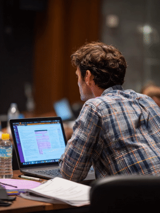 Man working on a laptop with documents and a water bottle on a desk.