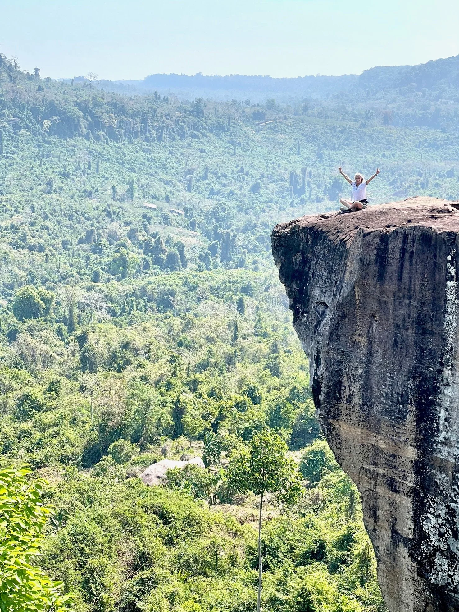 Mary Bridget Hart from Yoga with Hart sits at the edge of a cliff in a beautiful green landscape