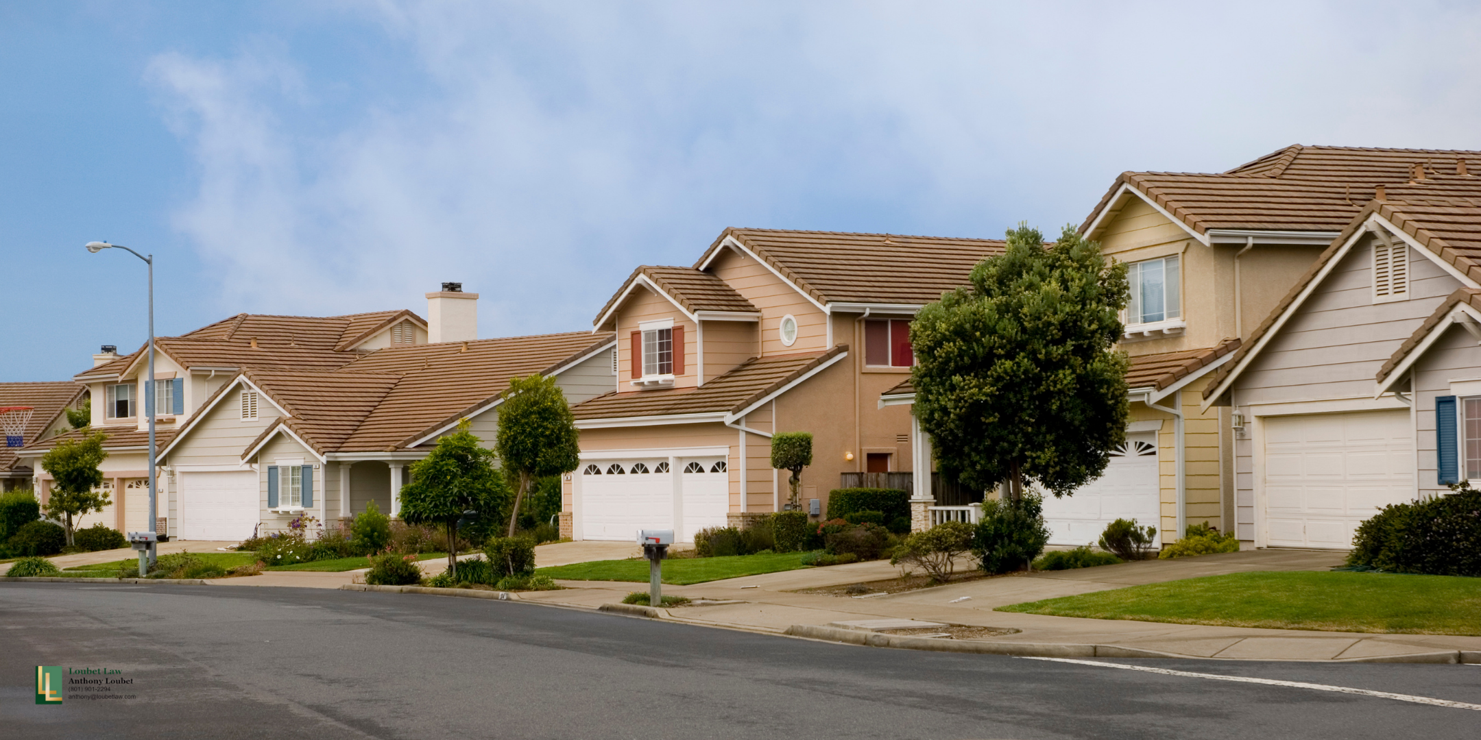 Residential neighborhood with single-family houses, well-maintained lawns, trees, a street with a sidewalk, and a mail carrier mailbox.