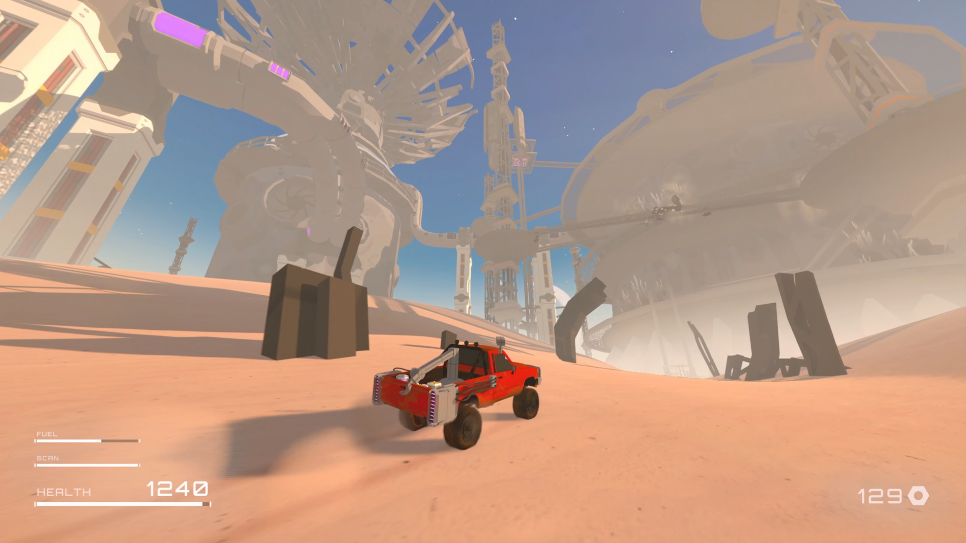 A red vehicle in a desert landscape with futuristic, large industrial structures in the background, under a clear blue sky.