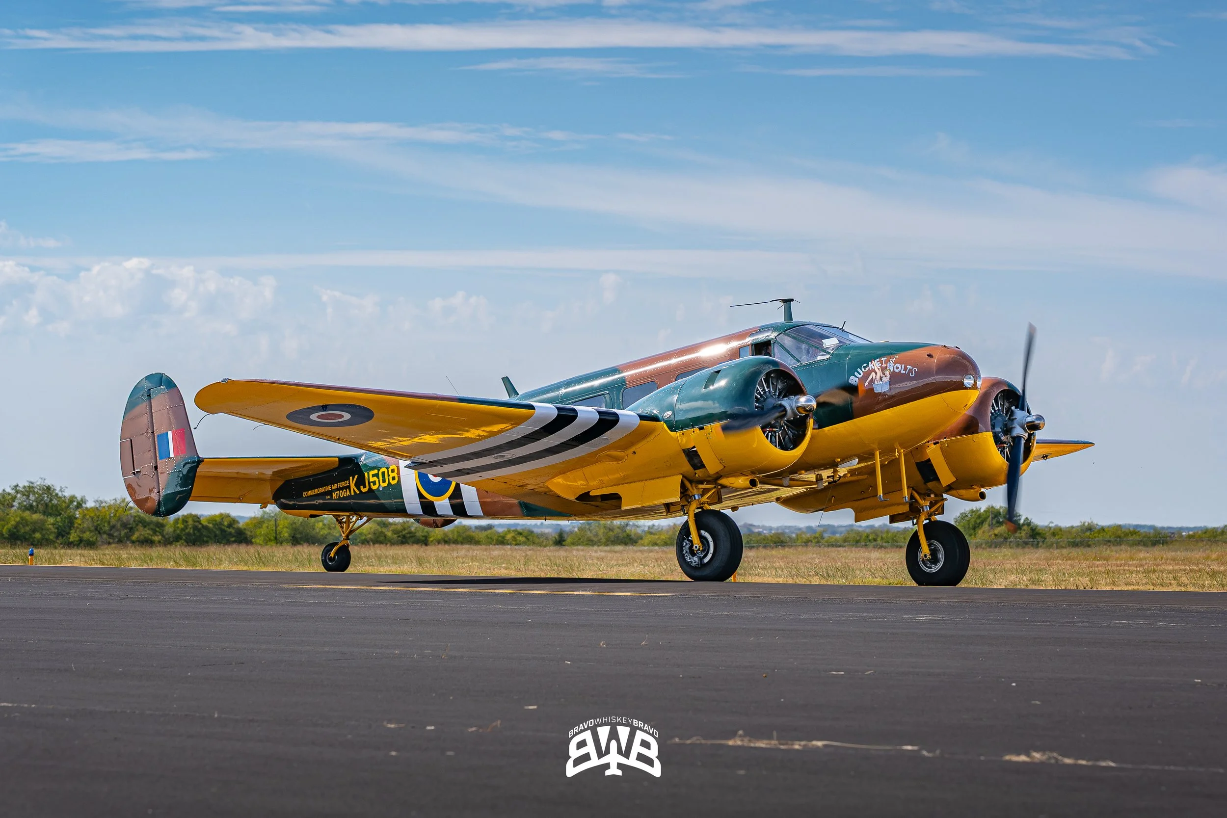 Colorful vintage airplane on runway with blue sky and clouds in background.