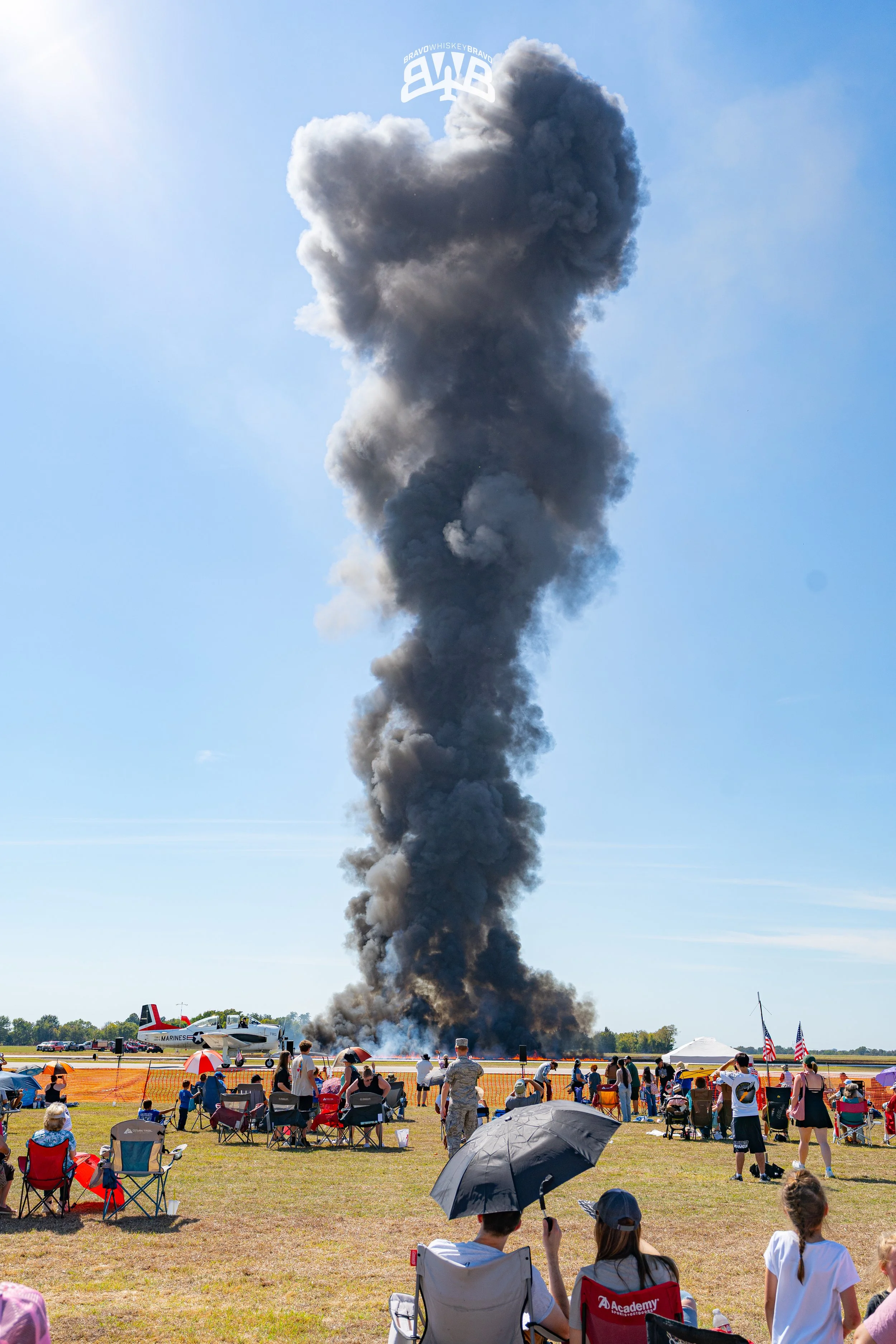 A plane crash with a large plume of smoke, and people watching from the ground at an airshow.