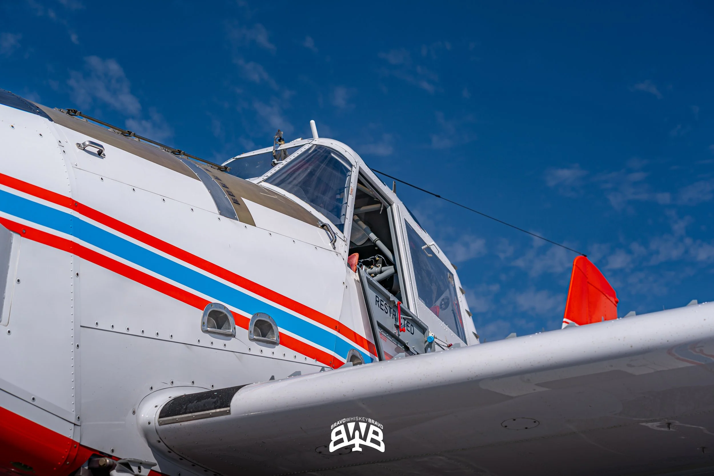 Close-up of a white and red aircraft with a cockpit and canopy, against a clear blue sky.