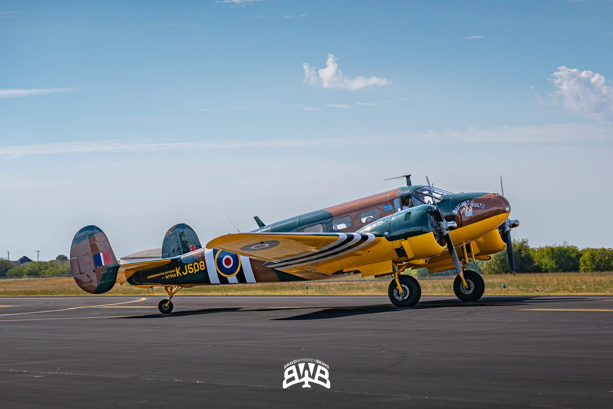 A vintage military aircraft with a green and yellow body, parked on a runway under a blue sky with some clouds.