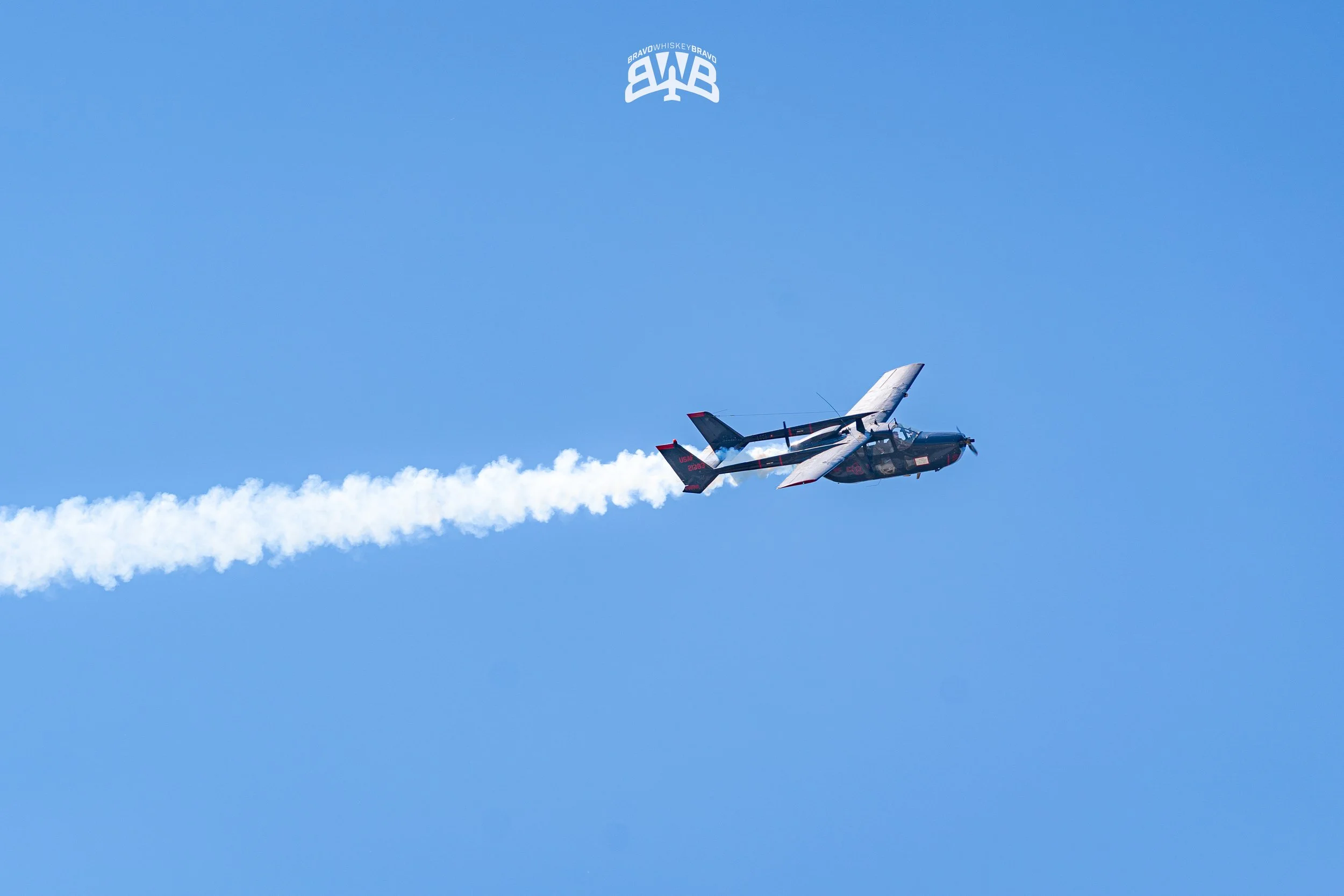 A Black Hawk helicopter flying in a clear blue sky, releasing a white smoke trail.