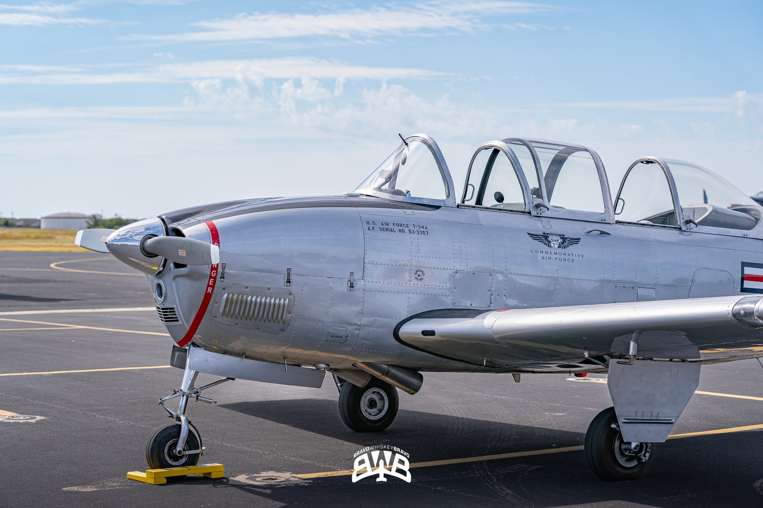 A vintage military aircraft parked on an airfield tarmac during daytime, with a clear sky and some clouds in the background.