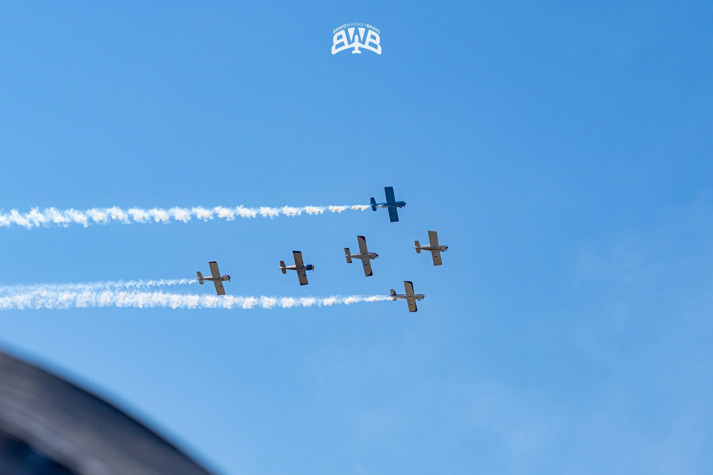 Six aircraft flying in formation against a blue sky, with white vapor trails.