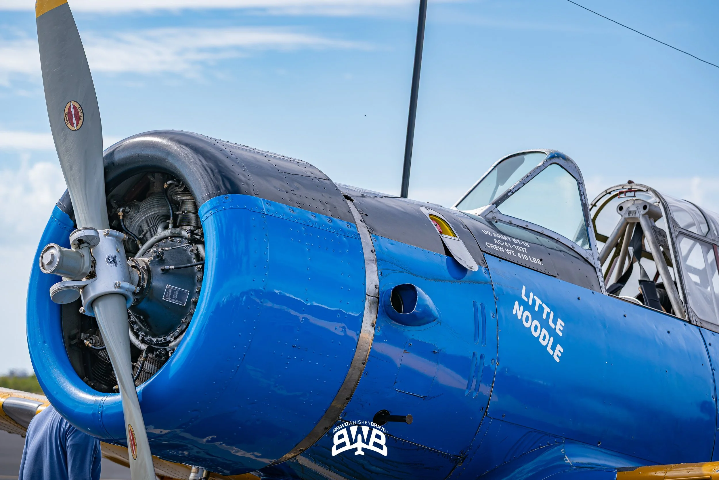 Close-up of a vintage blue and silver aircraft engine and nose, with the cockpit visible and the name 'Little Noodle' painted on the side.