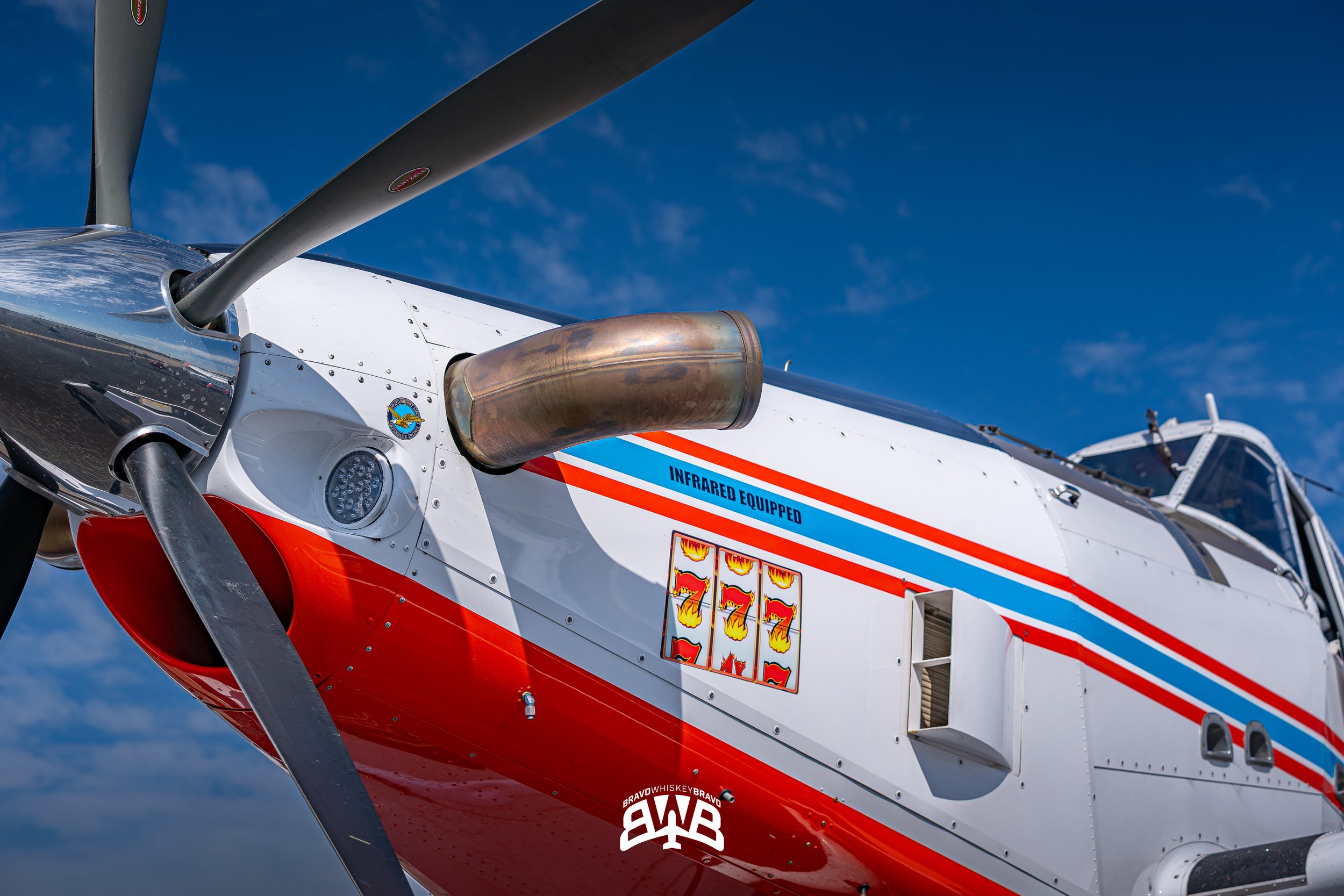 Close-up view of a helicopter's nose, showing its propeller and a metallic exhaust pipe, with a blue sky in the background.