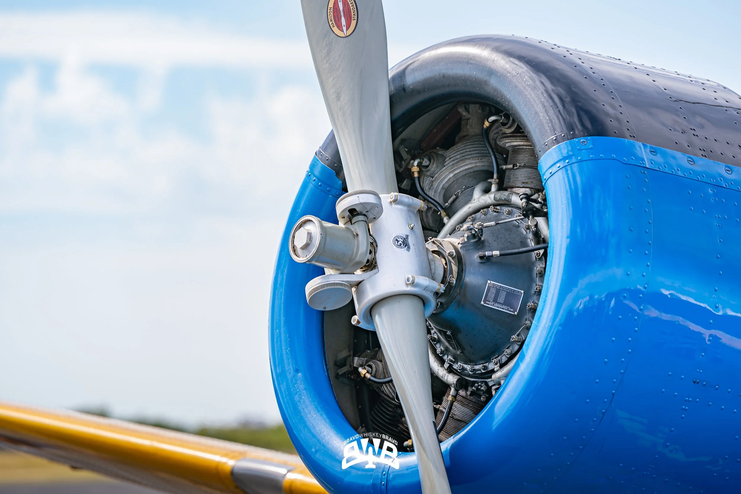 Close-up of a vintage airplane engine and propeller on a blue aircraft with a yellow wing, under a partly cloudy sky.