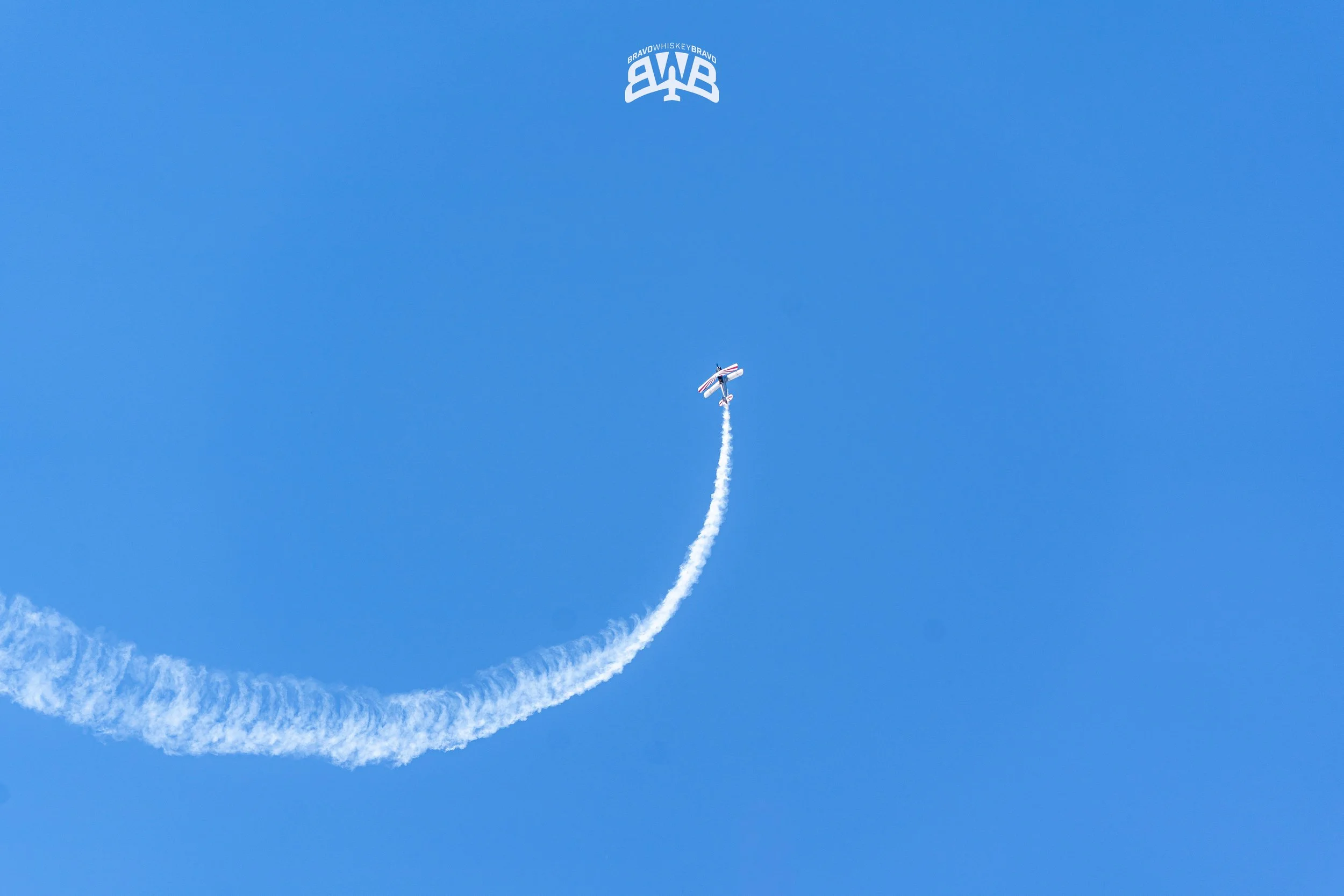 An airplane performing an aerobatic stunt against a clear blue sky, leaving a white smoke trail behind.