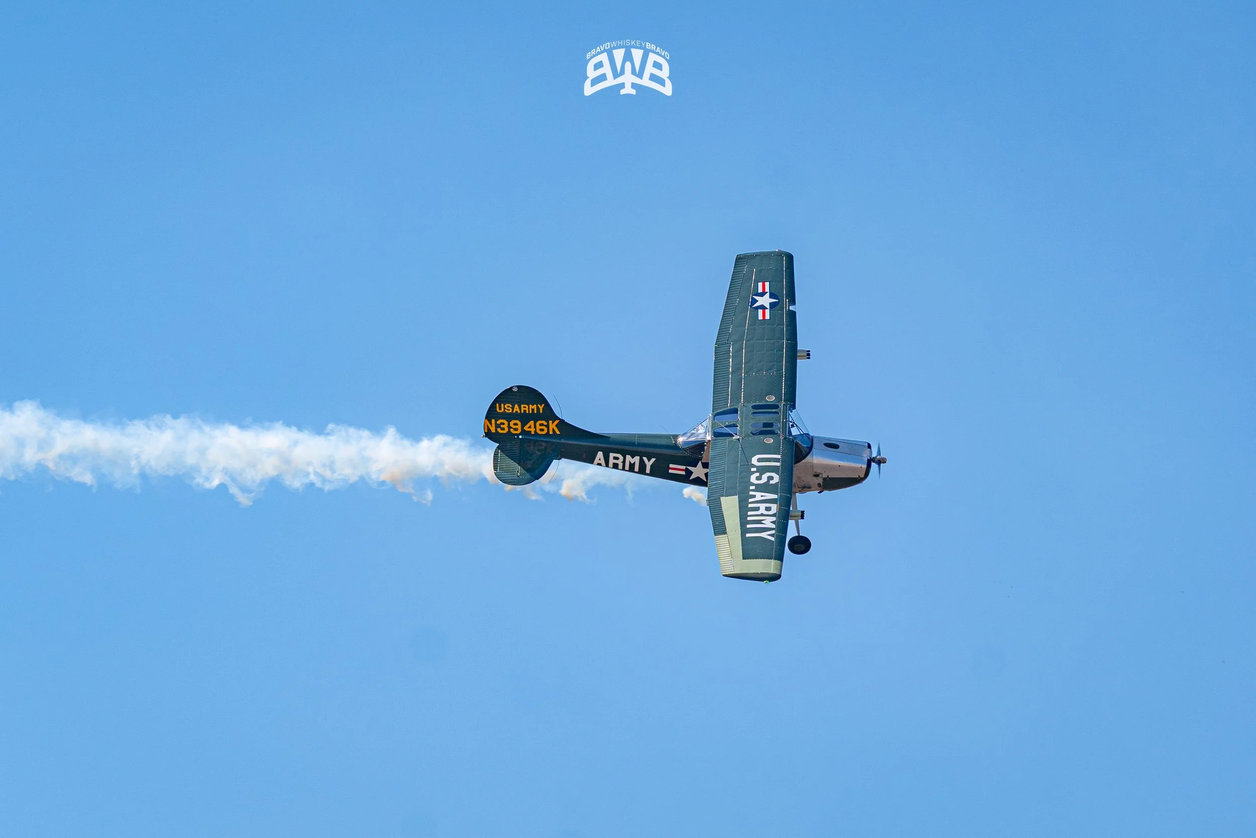 An aircraft painted in U.S. Army markings flying in the sky with a trail of white smoke behind it.