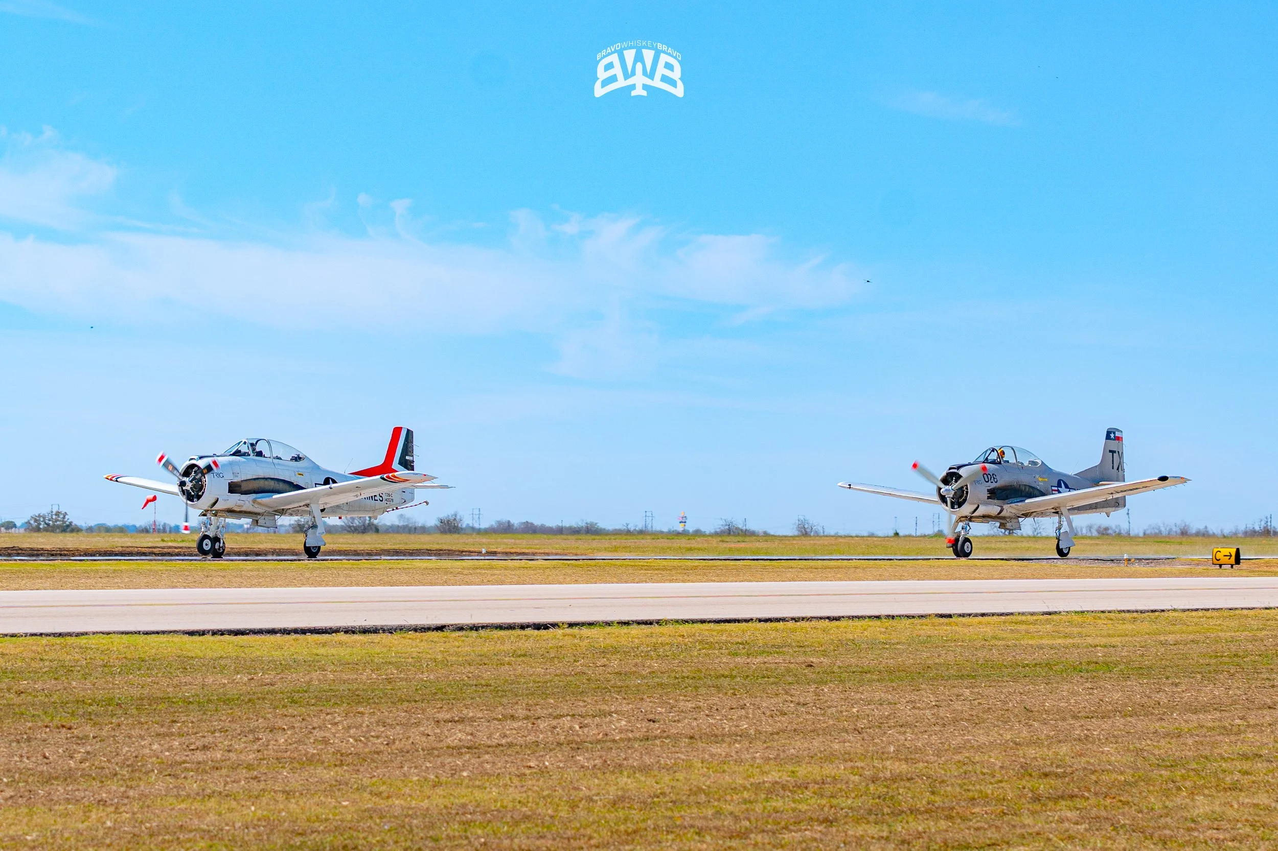 Two vintage military airplanes on a runway during daytime with a blue sky and light cloud cover.
