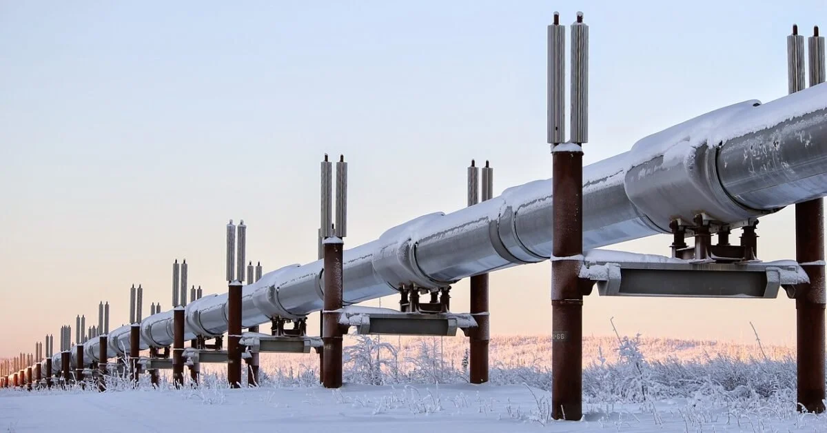 Large industrial pipeline running through a snow-covered landscape in winter, with a pale sky in the background.