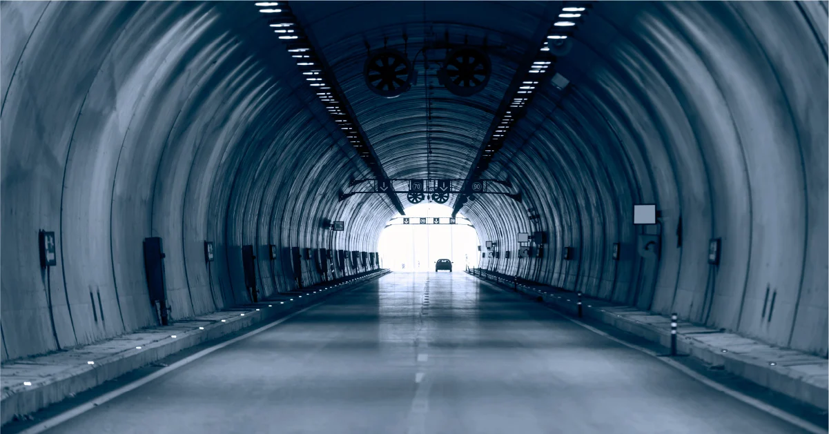 View inside a vehicle tunnel with a car approaching the exit at the end.