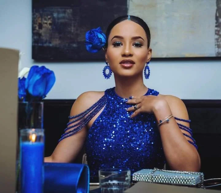 Une femme élégante portant une robe bleue brillante, avec des accessoires assortis, assise à une table.