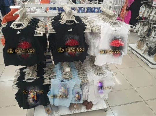 Vêtements pour enfants avec des motifs de crowns et de lèvres rouges, principalement en noir, blanc et bleu, sur une étagère en magasin.