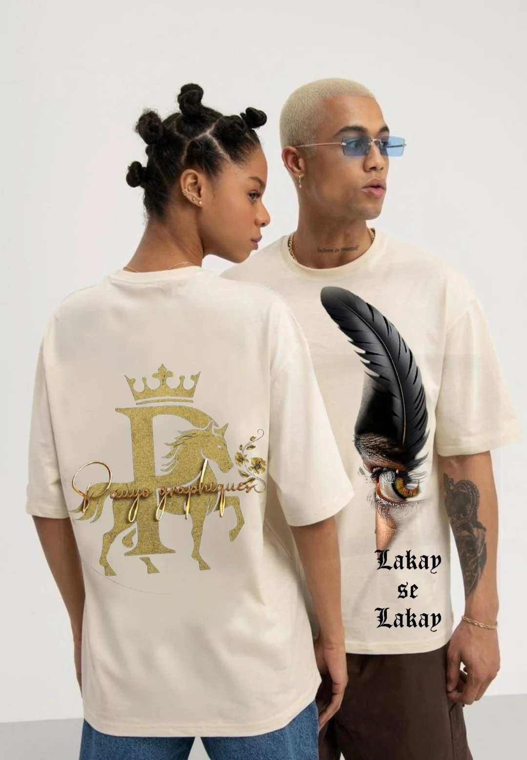 Deux personnes portent des t-shirts beige avec des dessins et des textes, l'un avec une licorne dorée sous une couronne, l'autre avec un œil et une plume noire, avec le texte "Lakay se Lakay".