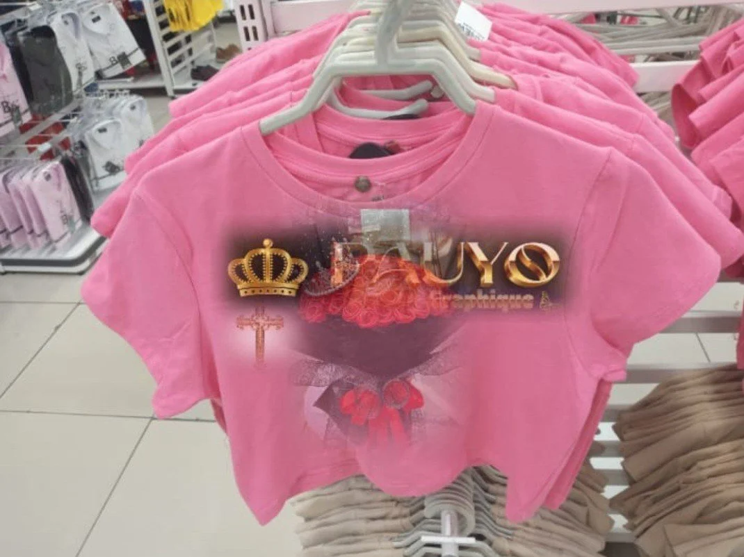 T-shirt rose avec un design de cœur et une couronne, affichant le mot 'BUY O' en or.