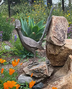 A garden sculpture of a heron standing on rocks, surrounded by various plants and orange flowers.