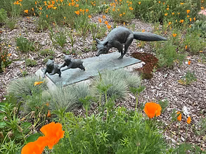 Squirrel sculptures on a rock among flowers and greenery in a garden.
