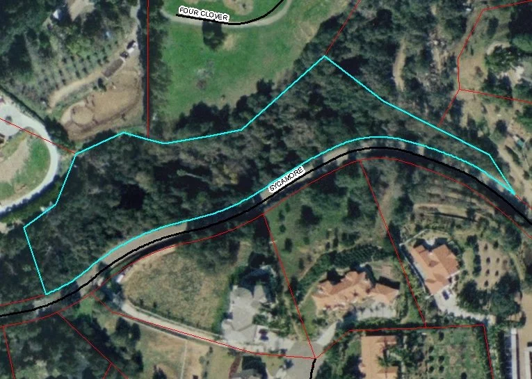 Satellite map showing a winding road labeled Sycamore, surrounded by residential homes, trees, and property boundaries.