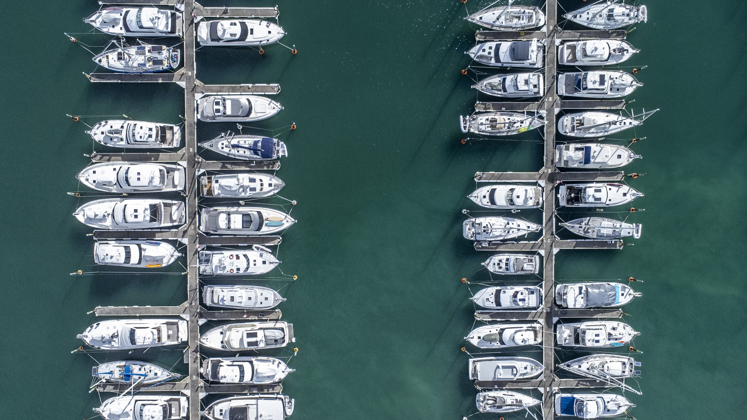 Aerial view of multiple boats docked at two parallel marinas in a body of water.
